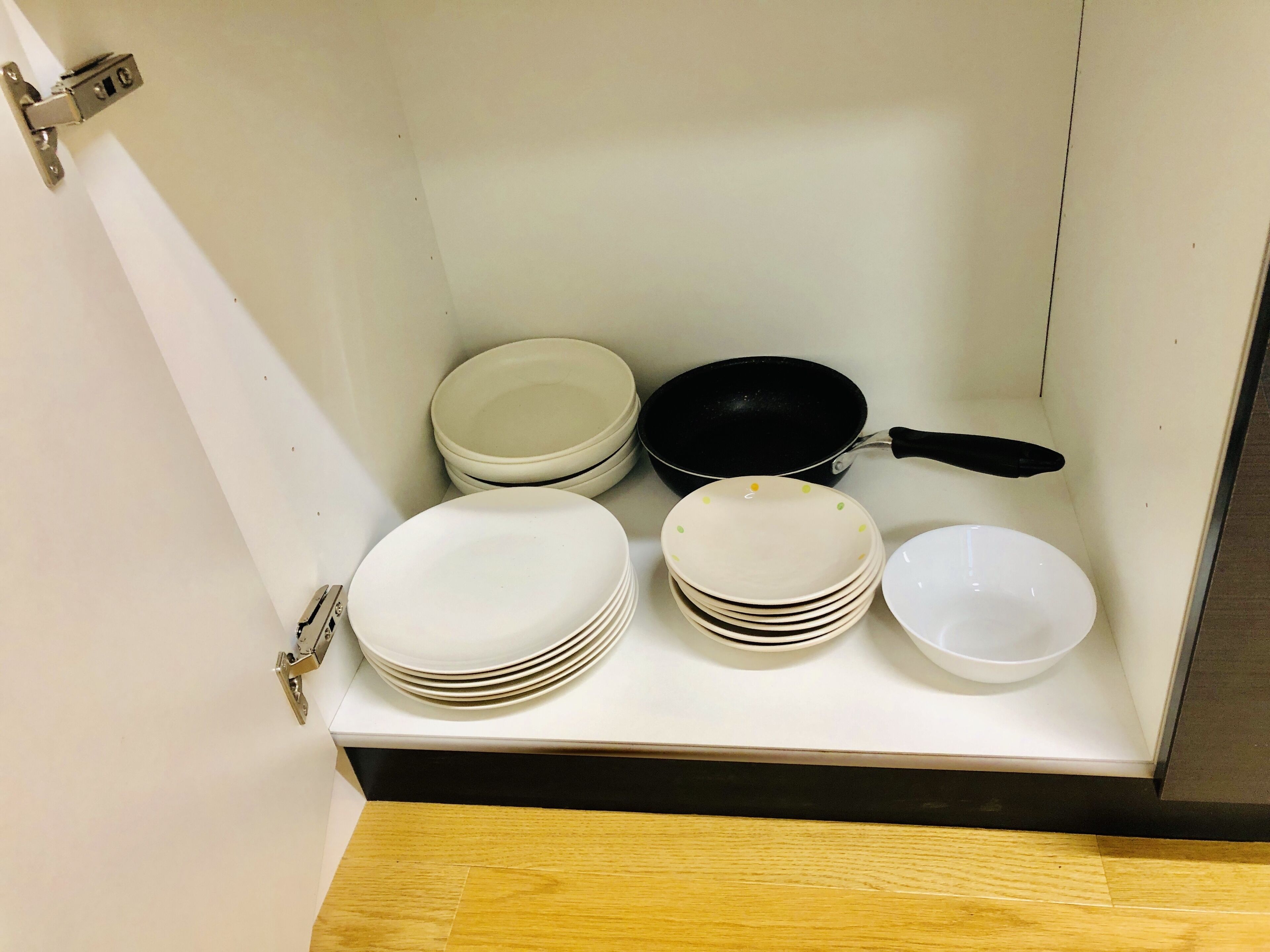 A kitchen cabinet with white plates, bowls, and a black frying pan.