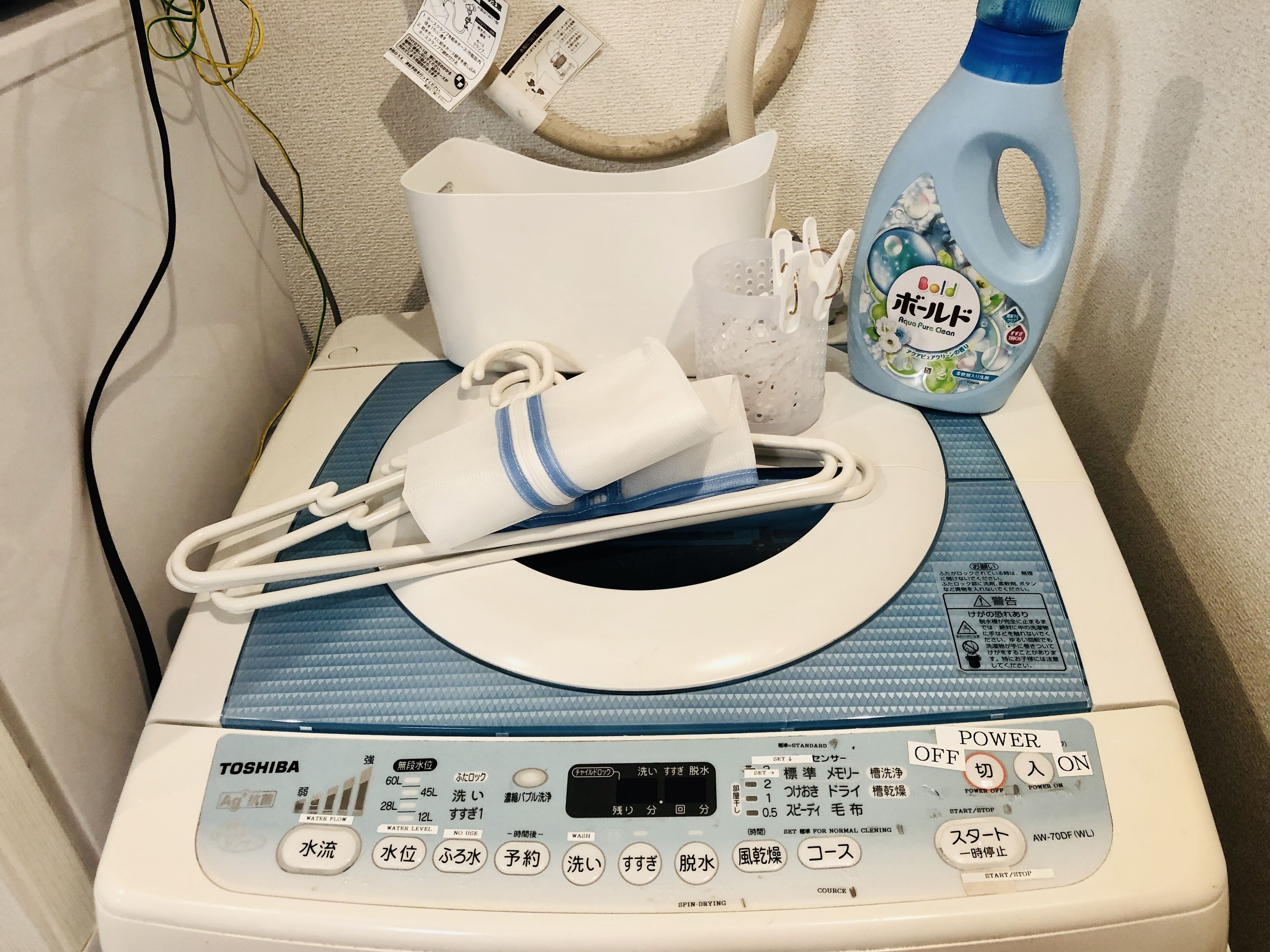 Una rentadora Toshiba amb un panell de control, un drap blanc i una ampolla de detergent.