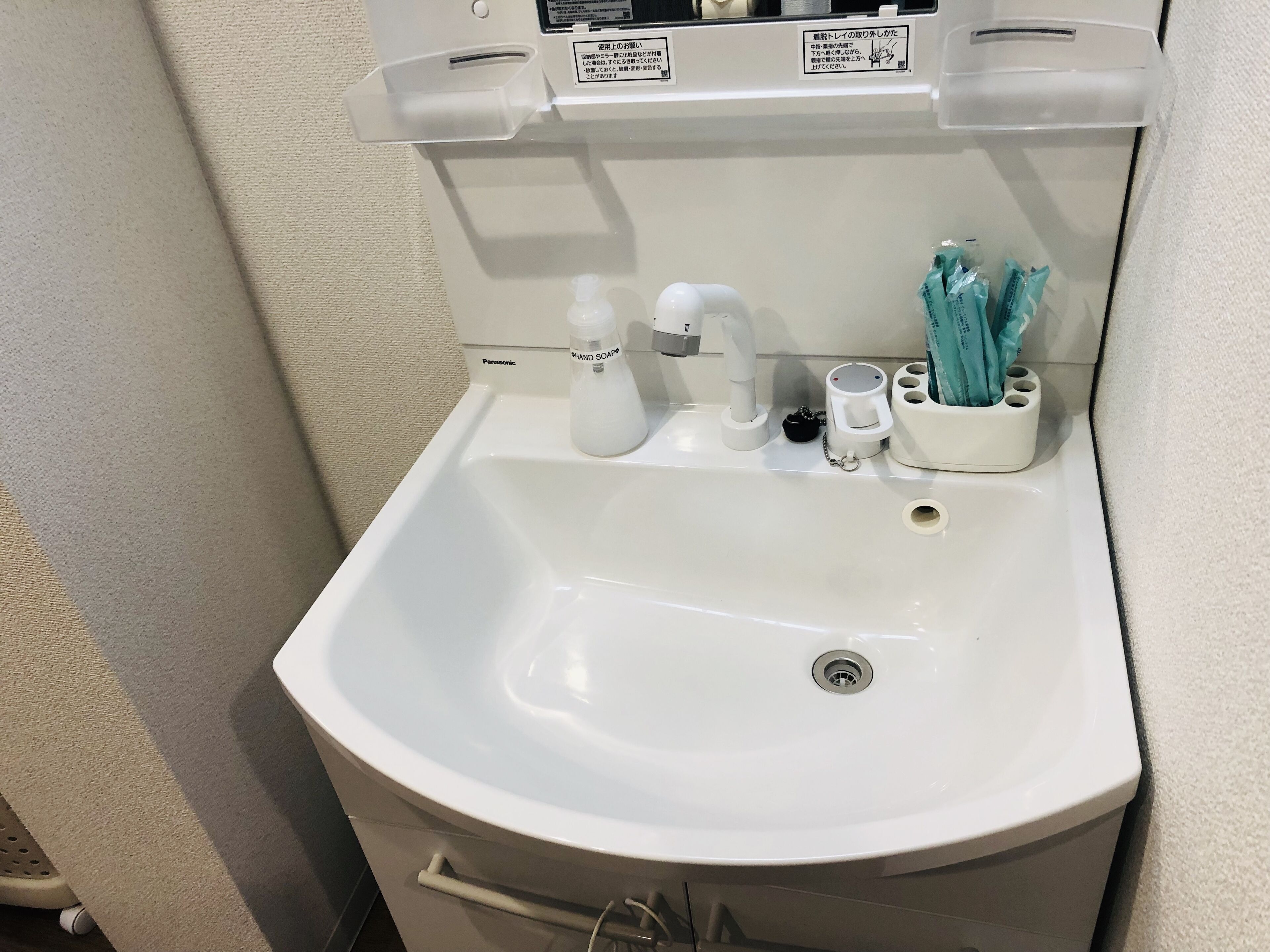 A white bathroom sink with a handheld soap dispenser, a faucet, and a cup holder.