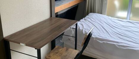 A compact room with a foldable desk, a chair, a bed, and a window with curtains.