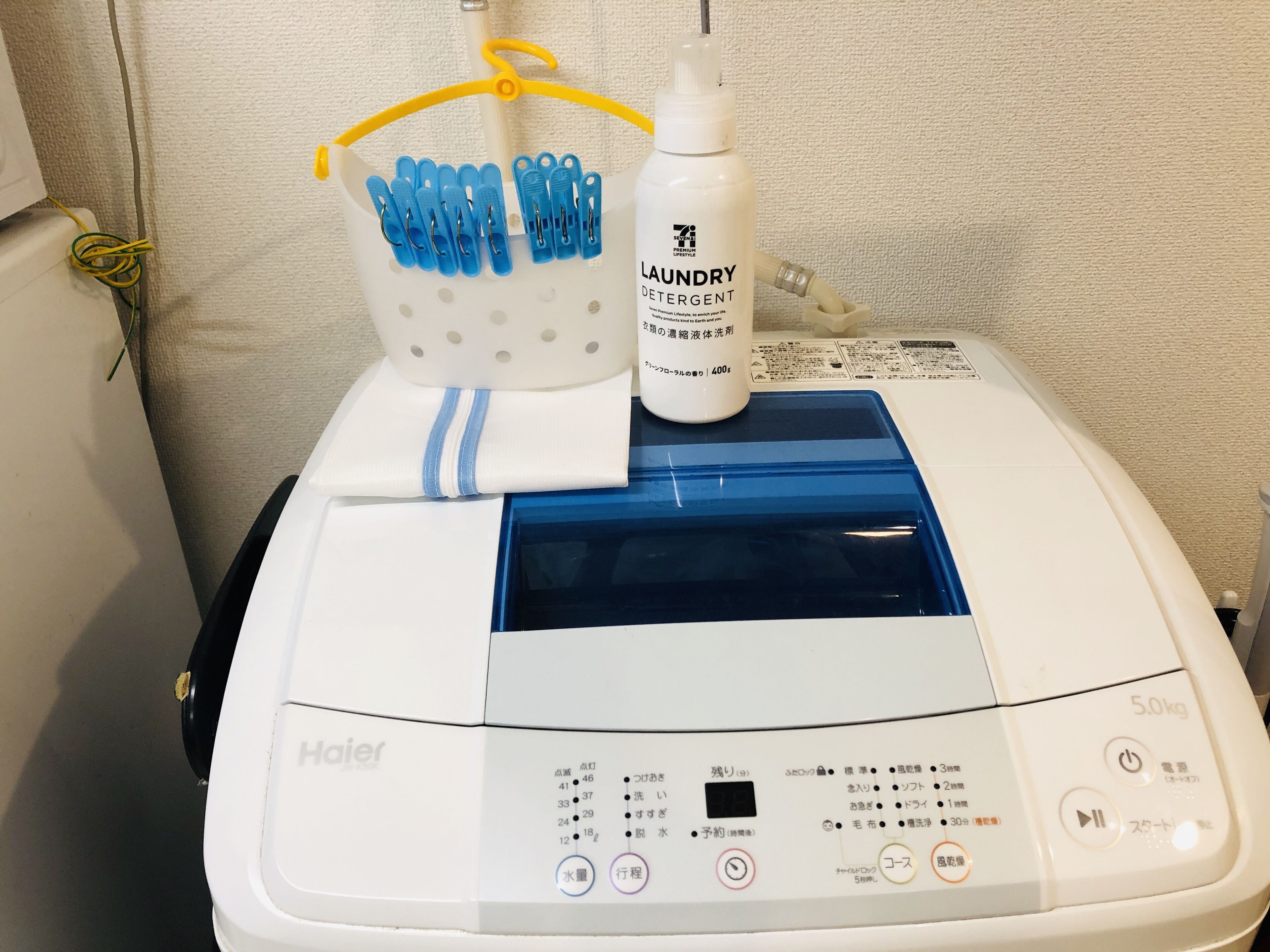 A white Haier washing machine with a blue control panel, a detergent bottle, and a blue clothespin holder.