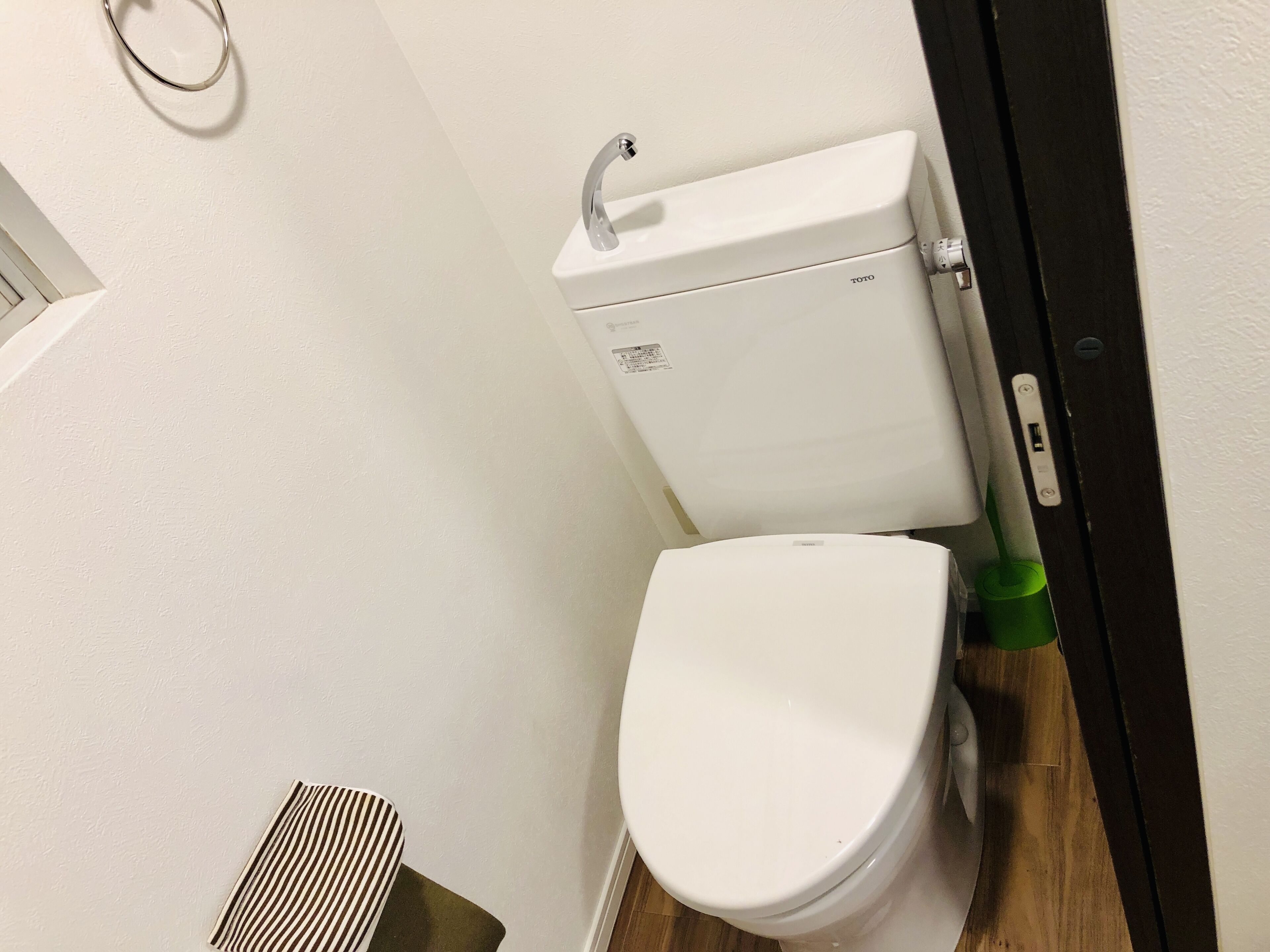 A white toilet with a TOTO brand label, a green cleaning brush, and a wooden floor.