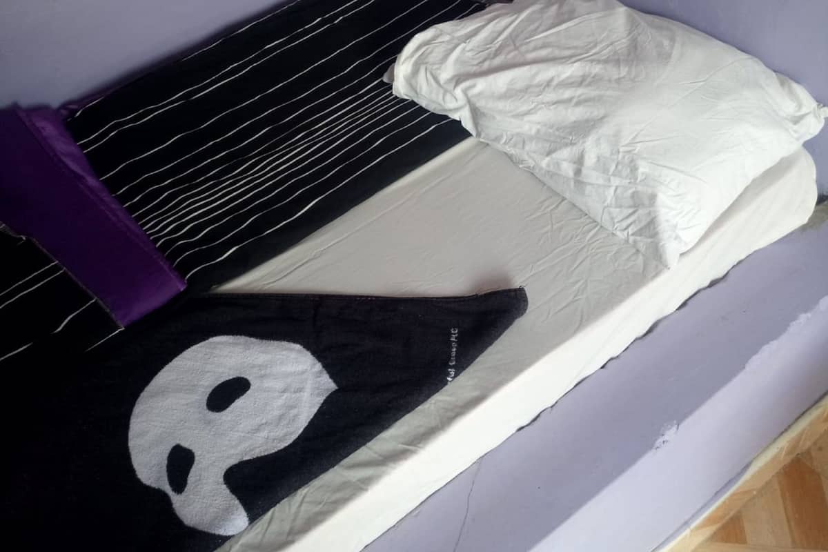 Une petite chambre avec un lit simple, dotée d’un matelas rayé noir et blanc, d’un oreiller blanc et d’une couverture noire et blanche.