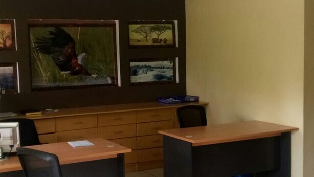 A conference room with a high ceiling, wooden desks, and chairs, and artwork on the walls. - Moonlight Bar & Lodging (Nakuru)