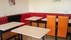 A restaurant interior with red and black cushioned booths, beige tables, and orange chairs. - Moonlight Bar & Lodging (Nakuru)