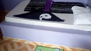 A bed with a black and white striped pillow, a white pillow, and a purple pillow. There is a pair of blue flip-flops on a green mat. - Moonlight Bar & Lodging (Nakuru)