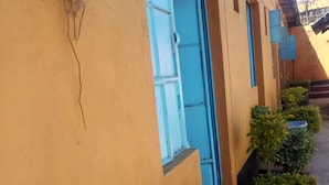 A building with yellow walls and blue window frames. There are small green bushes in front of the building. - Moonlight Bar & Lodging (Nakuru)