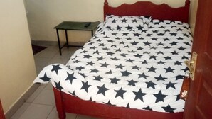 A single bed with a star-patterned bedspread in a room with a tiled floor and a small table. - Tausi Bar & Lodging (Nakuru)