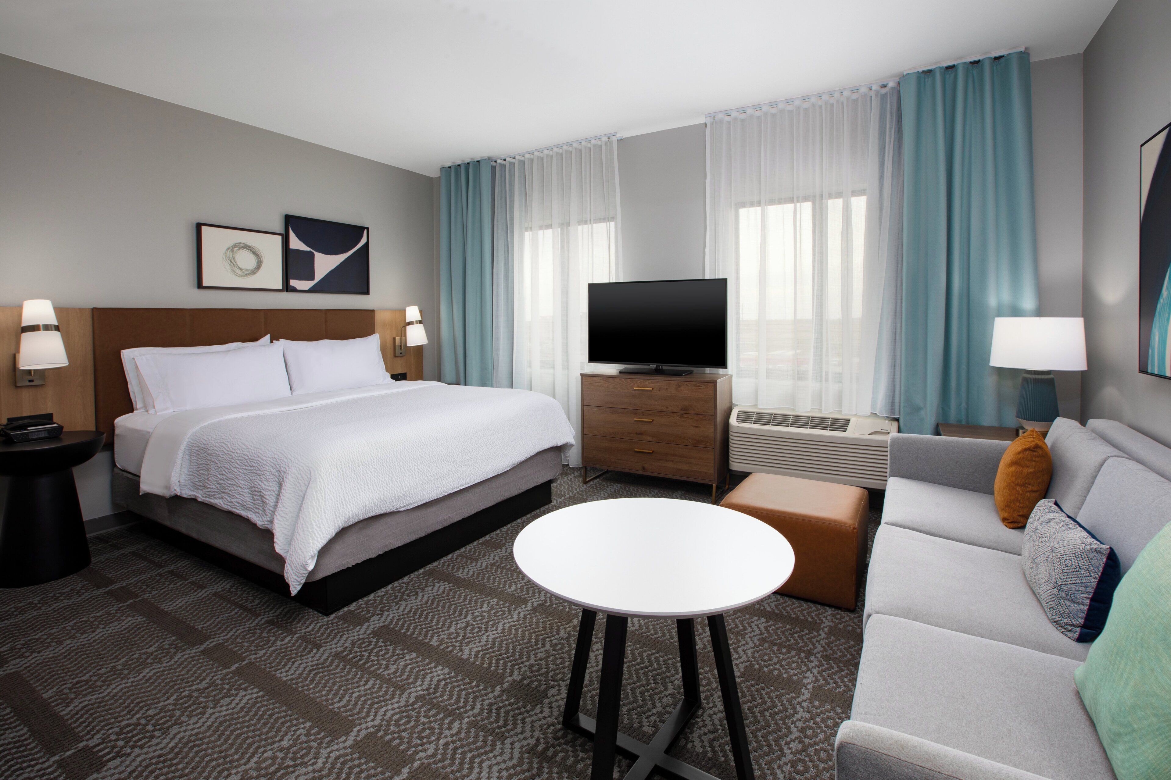 A hotel room with a bed, a TV, a sofa, a coffee table, and a desk with a lamp.