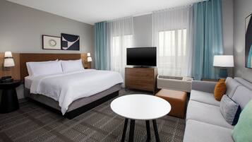 A hotel room with a bed, a TV, a sofa, a coffee table, and a desk with a lamp.
