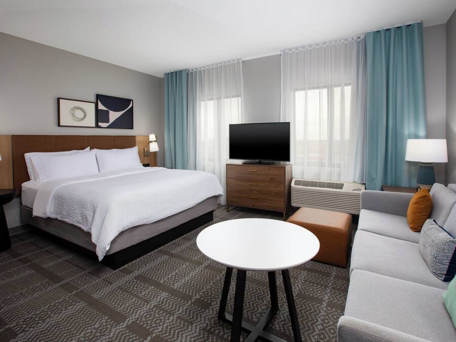 A hotel room with a bed, a TV, a sofa, a coffee table, and a desk with a lamp.