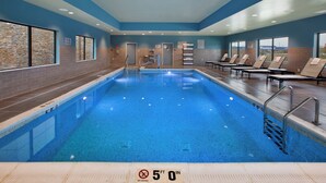An indoor swimming pool with clear lane markings, a diving board, and lounge chairs along the poolside. - Staybridge Suites Ames by IHG (Ames)