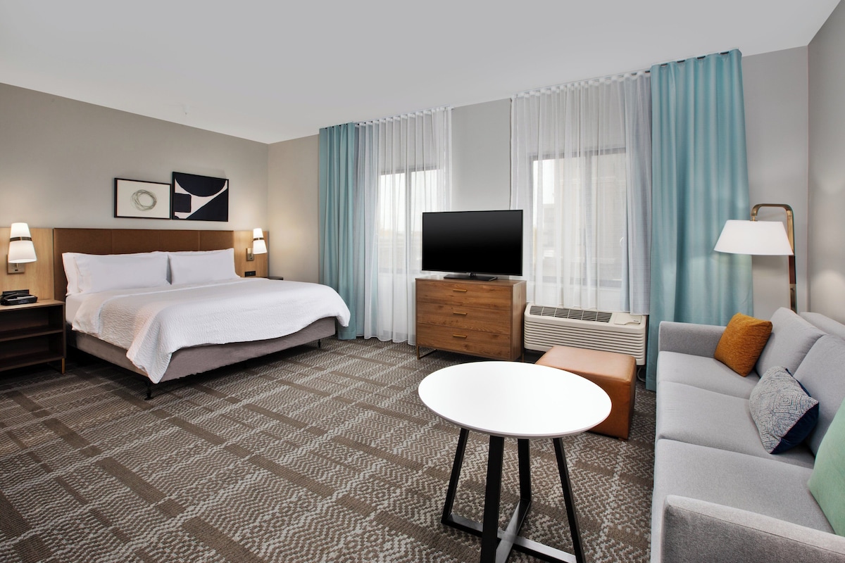 A hotel room with a bed, a TV, a sofa, a table, and a dresser.