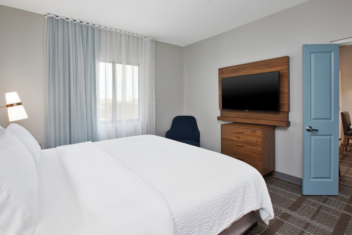 A hotel room with a large bed, a television mounted on the wall, a desk with drawers, and a door.