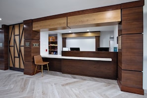 A reception area with a wooden reception desk, a brown chair, and a herringbone-patterned floor. - Staybridge Suites Ames by IHG (Ames)