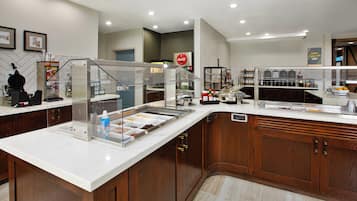 Una barra de desayuno con diversas opciones de comida, un refrigerador de Coca-Cola y una estación de café.