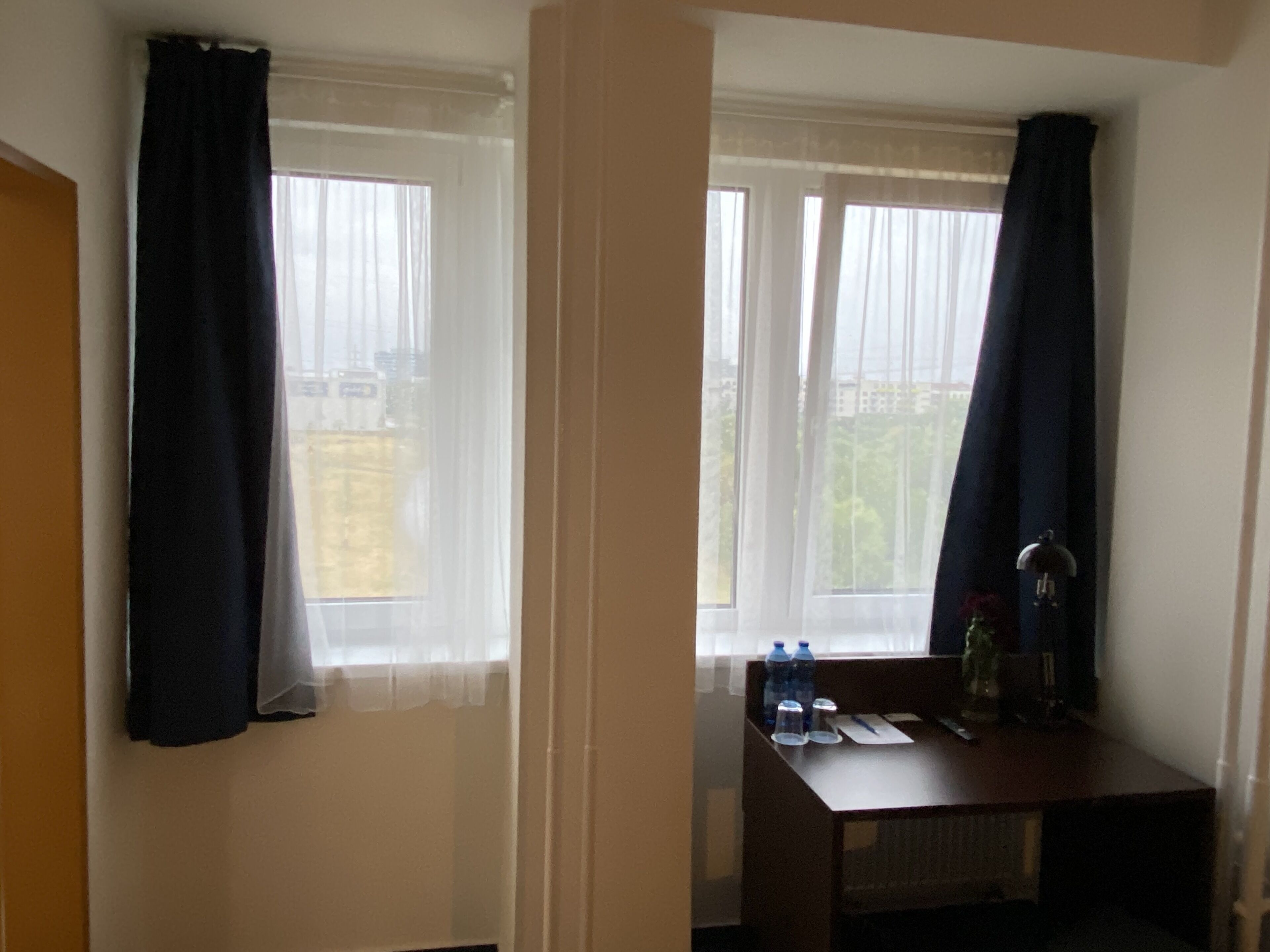 Ein Hotelzimmer mit zwei Fenstern, einem Holztisch mit Wasserflaschen und einem Heizkörper.