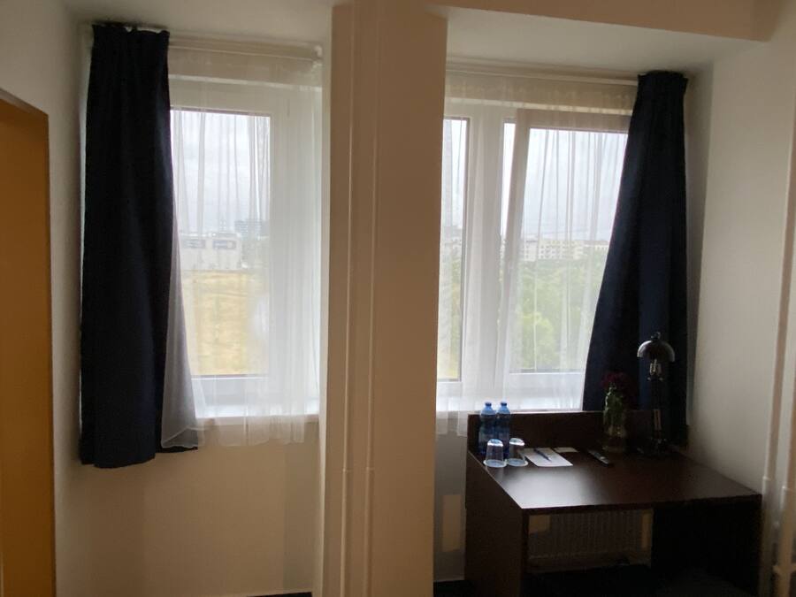 Habitación de hotel con dos ventanas, un escritorio de madera con botellas de agua y un radiador.