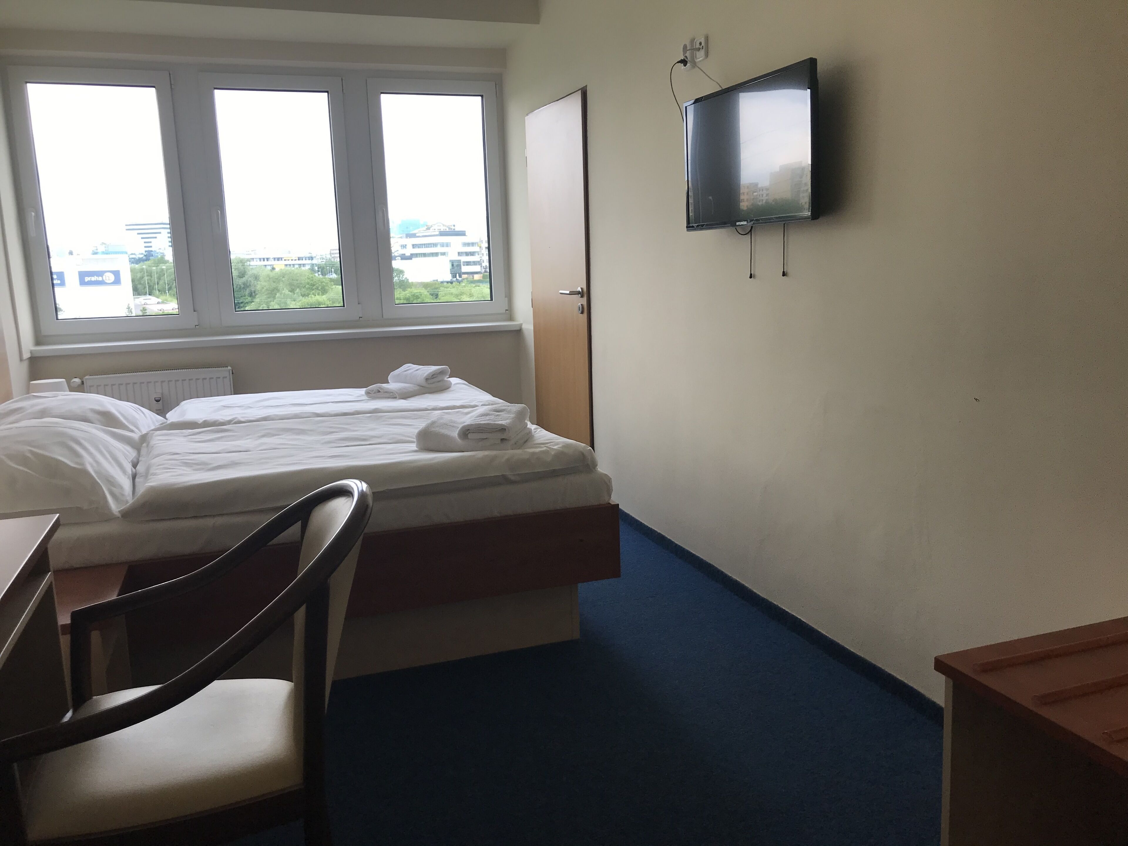 Habitación de hotel con cama, escritorio, silla, televisor y ventana con vistas a edificios.