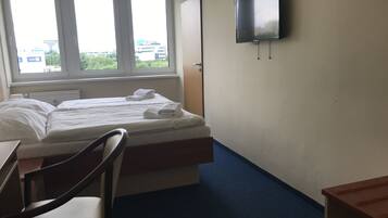 Habitación de hotel con cama, escritorio, silla, televisor y ventana con vistas a edificios.