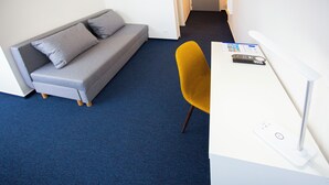 A room with a grey sofa, a yellow chair, and a white desk with a remote control. - HOTEL CHODOV ASC (Prague)
