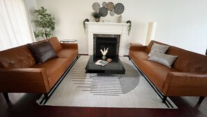 A living room with two brown leather sofas, a black coffee table, a white fireplace, and a patterned rug.