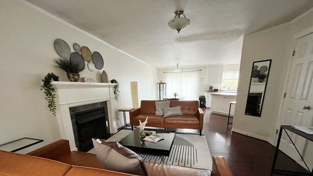 A living room with a fireplace, a brown leather sofa, a coffee table, and a dining area in the background.