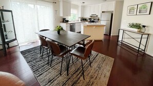A modern kitchen with white cabinets, a central island, and a dining area with a table and chairs.