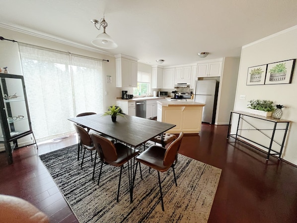 Une cuisine moderne avec des meubles blancs, un îlot central et un coin repas comprenant une table et des chaises.