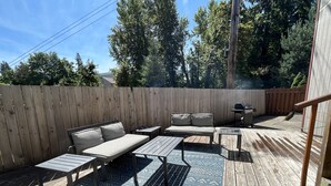 A wooden deck with a sofa, two tables, and a grill.
