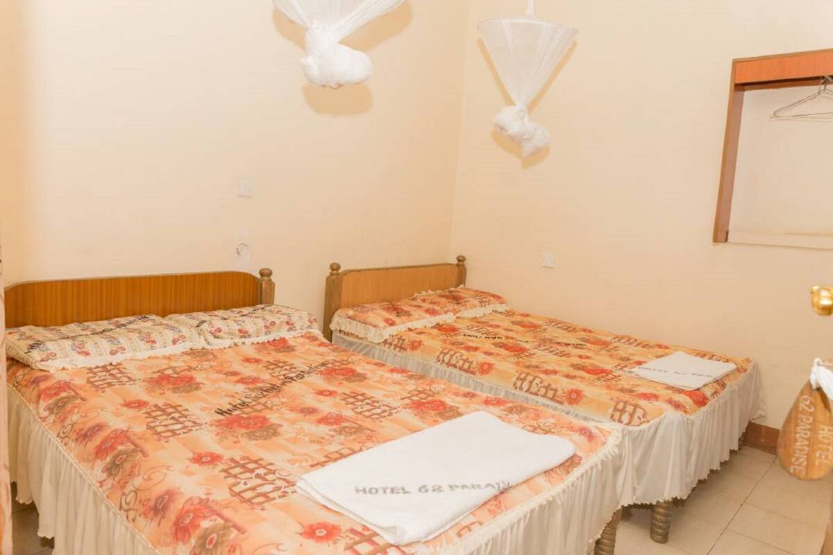 Habitación con dos camas, cabecera de madera, toalla blanca y mosquitero colgado.