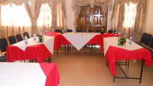 A conference room with tables covered in red and white tablecloths, equipped with water bottles and glasses, and surrounded by chairs. - Sixty Two Paradise Hotel (Nanyuki)