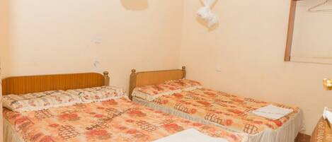 A hotel room with two beds, a wooden headboard, a hanging mosquito net, and a framed mirror on the wall.