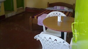 A room with a bed, a round table, and a white chair. - Mukuruwe-Ini Guest House (Marua)