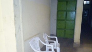 A corridor with white plastic chairs lined up against a wall, leading to a green door. - Mukuruwe-Ini Guest House (Marua)