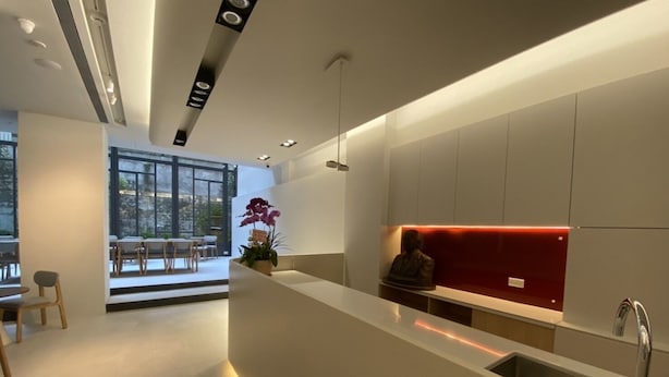 A modern kitchen with a central island, a red accent wall, and a view of an outdoor dining area. - Huru House (Taichung)