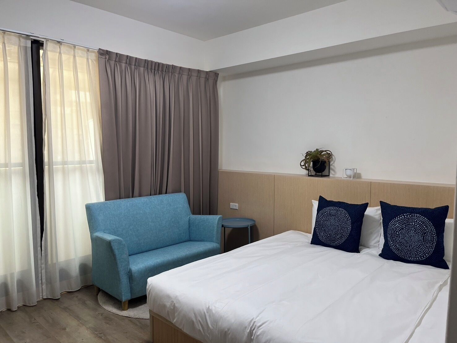 A hotel room with a bed, a blue armchair, a small round table, and a nightstand.