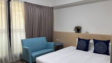 A hotel room with a bed, a blue armchair, a small round table, and a nightstand.