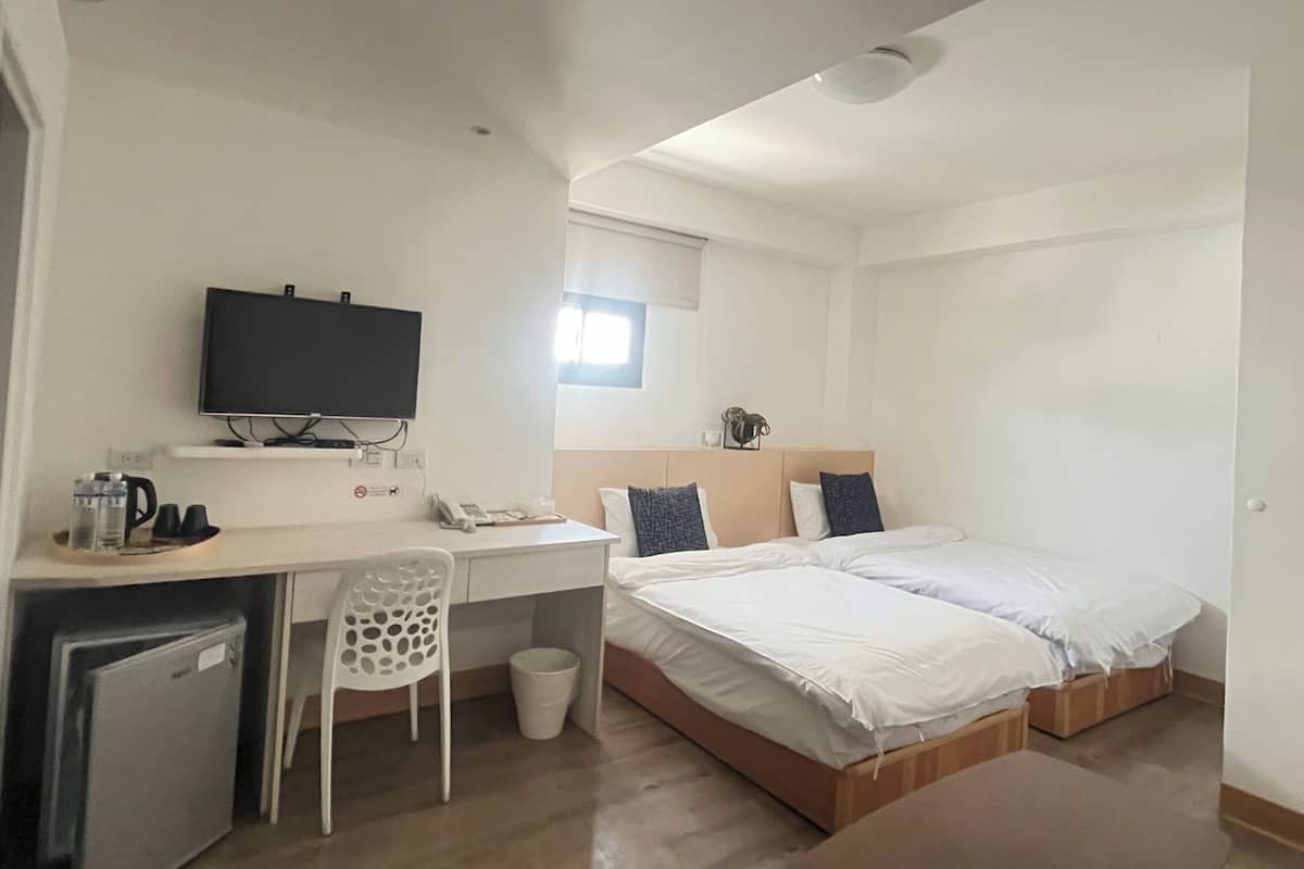 A compact hotel room with a single bed, a desk with a television, a small refrigerator, and a chair.