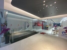 A modern hotel lobby with a glass partition, a reception desk, and a seating area with tables and chairs.