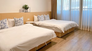 A hotel room with two single beds, a small bedside table, a potted plant, and a large window with sheer curtains. - Huru House (Taichung)