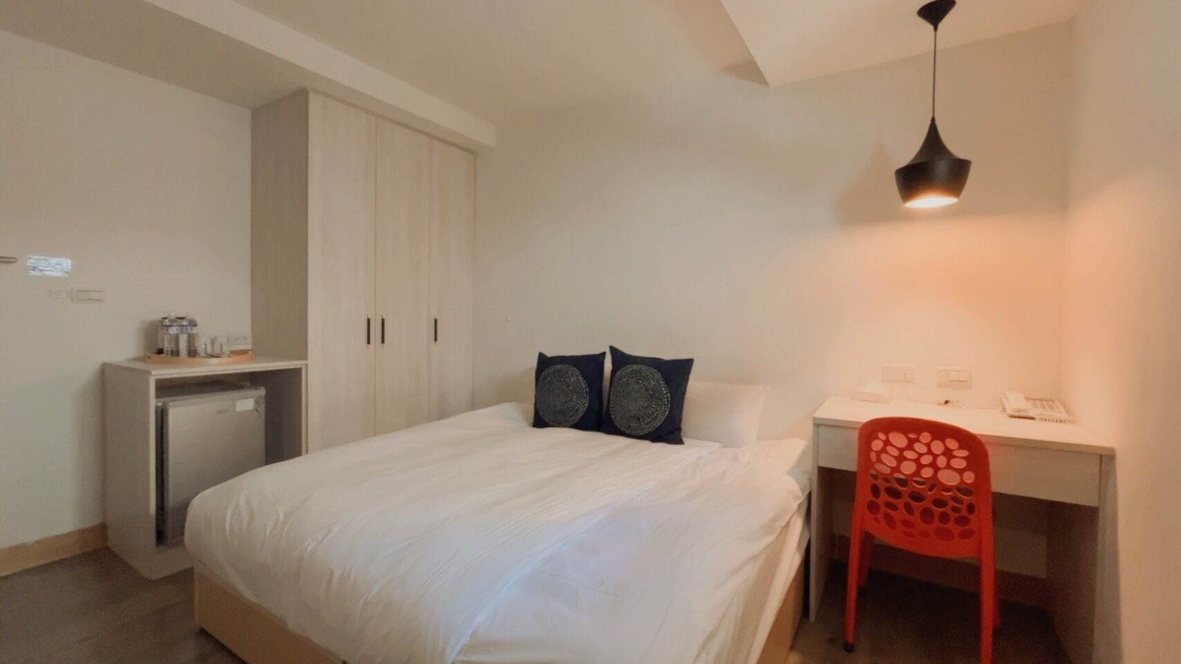 Un dormitorio con cama, escritorio, silla, armario y lámpara de techo.