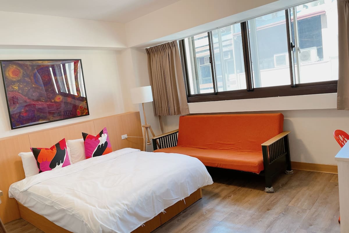 A hotel room with a bed, a sofa, a painting, and a window with curtains.