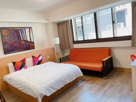 A hotel room with a bed, a sofa, a painting, and a window with curtains.