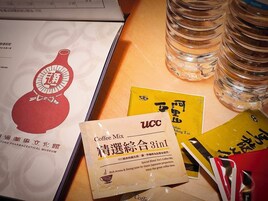 A table with a UCC Coffee Mix packet, a yellow booklet, and several clear bottles.