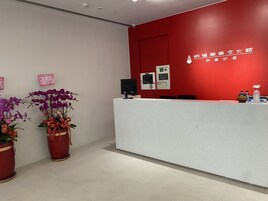 A reception desk with a red wall, two potted orchids, and a fire alarm on the wall.
