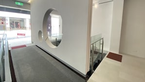 A modern interior with a glass railing, a circular mirror on the wall, and a staircase. - Huru House (Taichung)