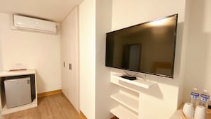 A modern hotel room with a flat-screen TV mounted on a white wall, a small refrigerator, and a wooden floor. - Huru House (Taichung)