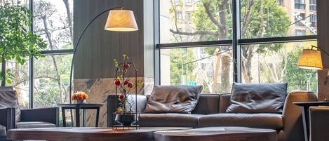 Un intérieur moderne avec un canapé en cuir, une table basse et deux lampadaires. De grandes fenêtres offrent une vue sur l’extérieur.