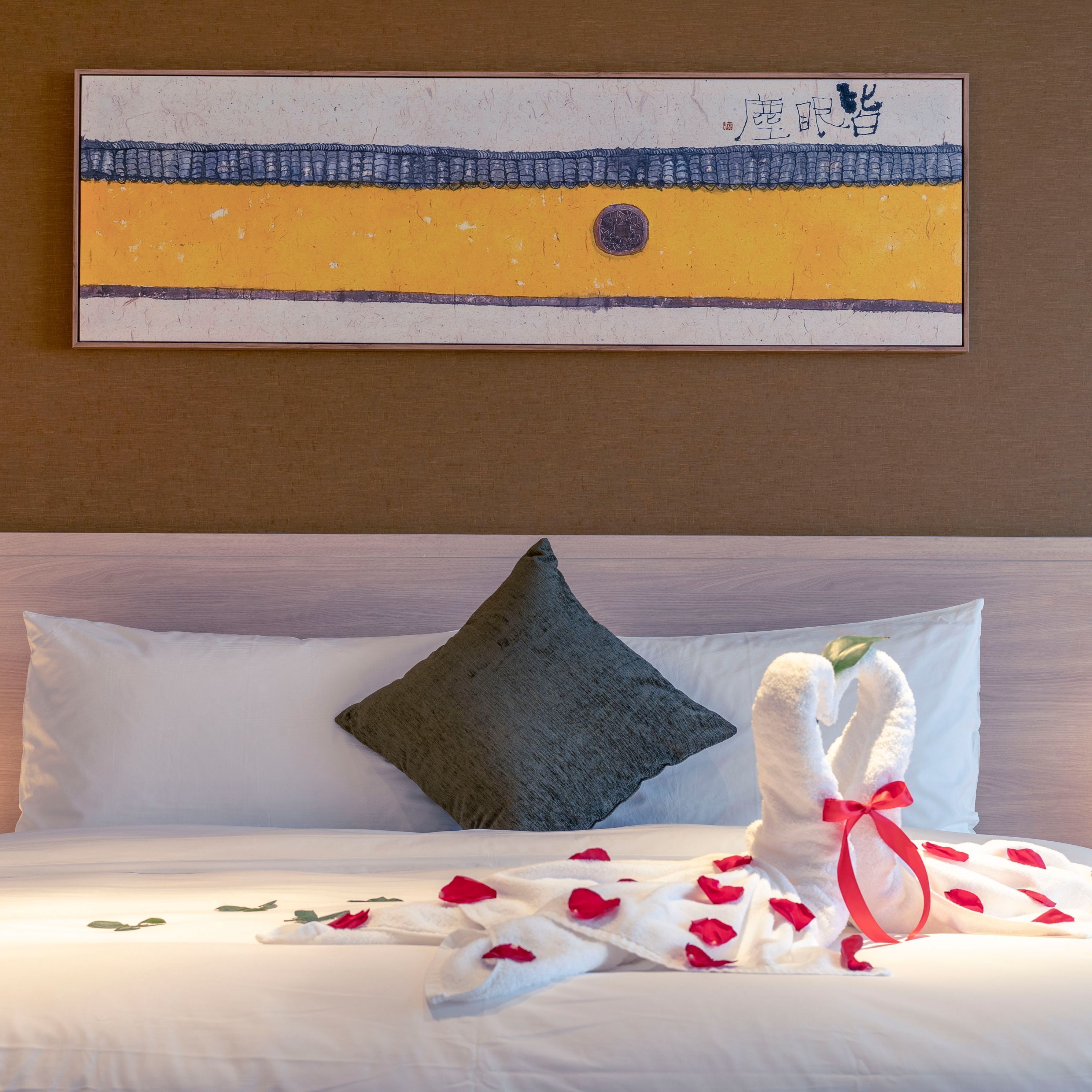 A hotel room with a bed, pillows, a decorative towel, and a painting on the wall.